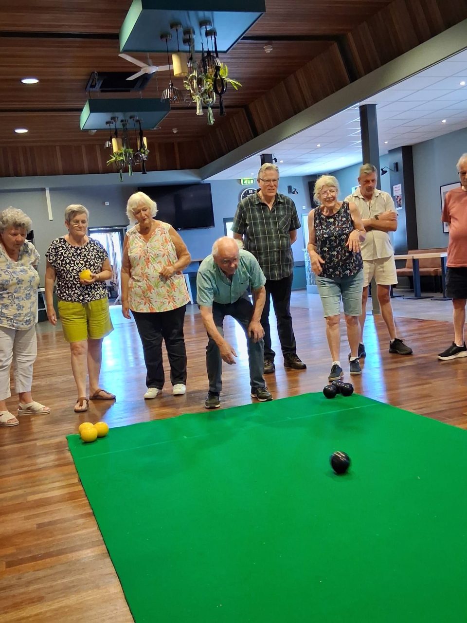 Senioren spelen jeu de boules op een groene mat in een recreatieruimte.